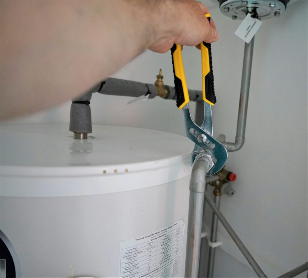 Person using pliers to adjust water heater pipe connection.