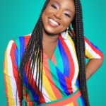 Smiling woman in colorful striped dress against teal background, looking confident and joyful.