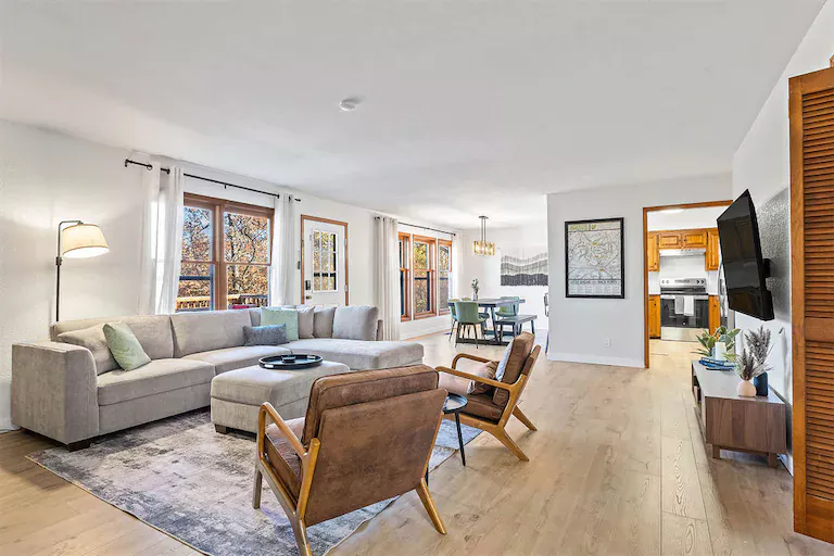 Spacious living room with modern decor, large windows, and cozy furniture, connected to an open dining area and kitchen.