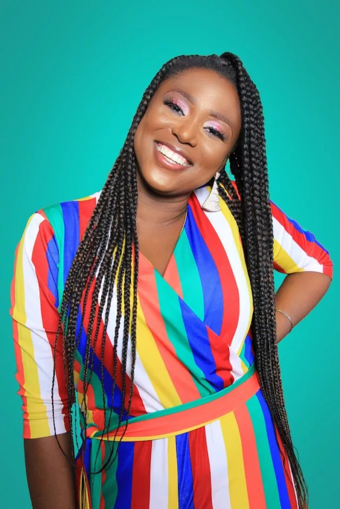 Smiling woman in colorful striped dress against teal background, looking confident and joyful.