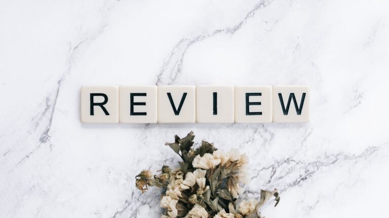 Scrabble tiles spelling 'REVIEW' on a marble surface with dried flowers.